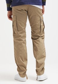 Beige cargobyxor i tyg, med flera sidofickor, avslappnad passform och lätt lyster. Bärs med vita sneakers.