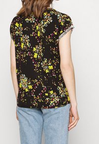 Czarna bluzka z krótkimi rękawami, zdobiona wielokolorowym wzorem kwiatowym. Materiał wydaje się miękki, ma luźny krój i zaokrąglony dół.