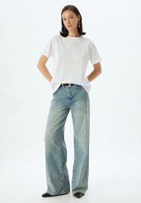 Hvid bomulds t-shirt med korte ærmer parret med løstsiddende lyseblå denim jeans. Sort bælte og sorte spidse sko.