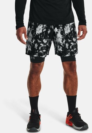 Uomo che indossa pantaloncini sportivi con motivo bianco e nero, con pantaloncini compressivi neri sotto, calzini neri e scarpe da corsa nere e rosse.