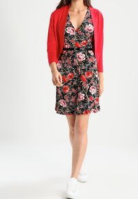 Kwiecista sukienka na czarnym tle, z różowymi różami i zielonymi liśćmi, połączona z czerwonym kardiganem. Całość dopełniają białe trampki.