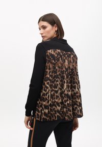 Černý pulovr s plisovaným leopardím potiskem na zadní straně. Přední část je jednobarevná, s límcem. Dlouhé rukávy a detail z texturované látky.