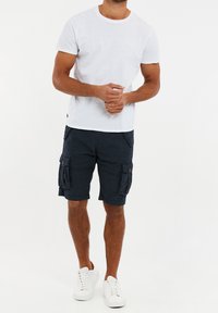 T-shirt bianco, pantaloni cargo blu navy con tasche laterali e sneakers bianche. Il tessuto sembra essere una miscela di cotone, con una vestibilità casual e rilassata.