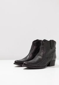 Botines negros de cuero texturizado, con un patrón escamoso, punta afilada y tacón corto cuadrado.