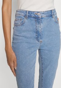 Jeans in denim azzurro chiaro con vita alta, cinque tasche, cuciture a contrasto e chiusura con bottone argentato. Tessuto liscio e design aderente.