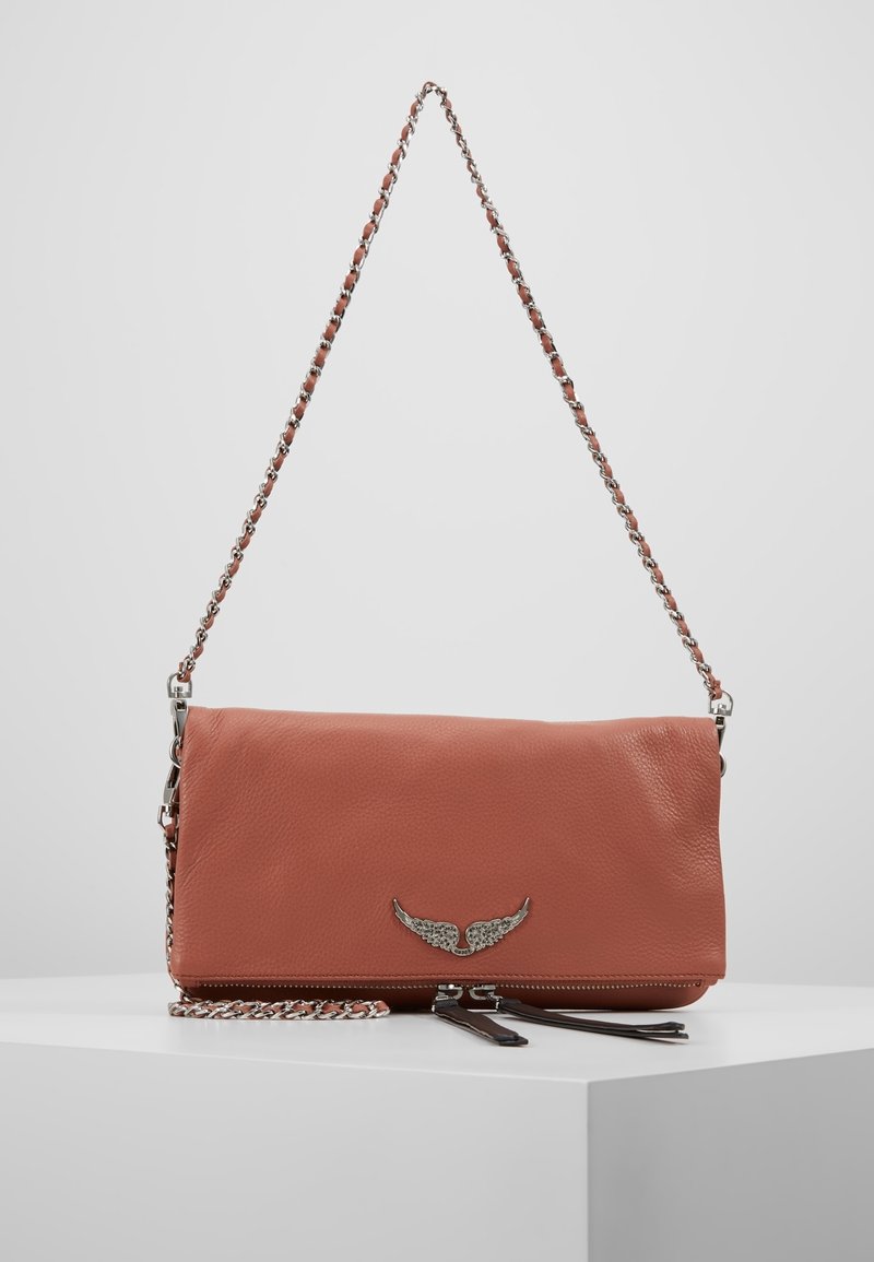 Skórzana torba na ramię w stonowanym koralu, z srebrnym okuciem w kształcie skrzydła, łańcuszkowym paskiem i zamykaną na zamek przegródką na dole.