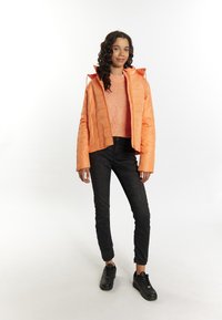 Korallfärgad puffjacka med en kort design och huva, tillsammans med en orange texturerad tröja, svarta slim fit-jeans och svarta sneakers.