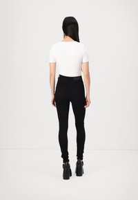 Pantalones negros de talle alto con piernas ajustadas, combinados con una blusa blanca de manga corta. El conjunto se complementa con tacones de plataforma negros.