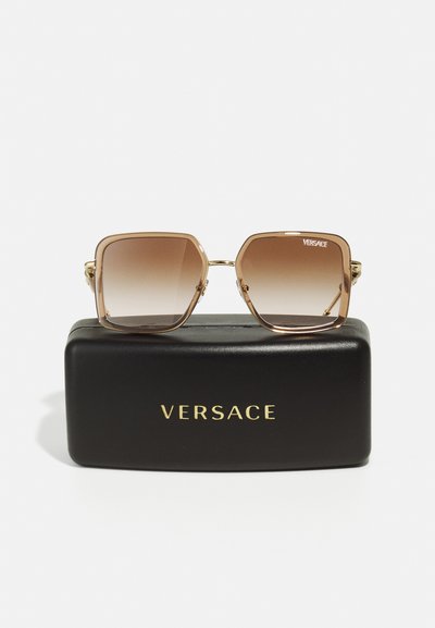Occhiali da sole quadrati Versace con lenti marroni sfumate, montatura in metallo e dettagli dorati. Presentati in un astuccio nero con scritte dorate.