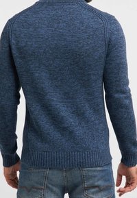 Granatowy sweter dziany o fakturowanym wzorze, z prążkowanymi mankietami i dołem oraz rękawami raglanowymi. Posiada standardowy okrągły dekolt.