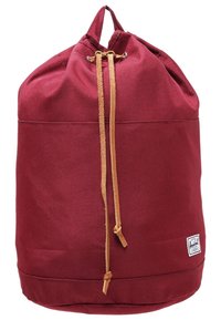 Burgundin värinen nyörilaukku, jossa on vaaleanruskeat nahkanyörit ja pieni valkoinen brändilogo alareunassa oikealla.