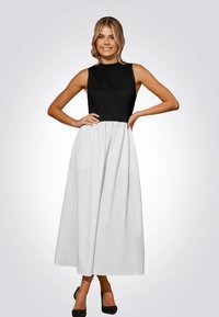 Robe maxi avec un corsage noir côtelé et une jupe blanche fluide. Texture lisse, design sans manches et détail de taille cintrée.