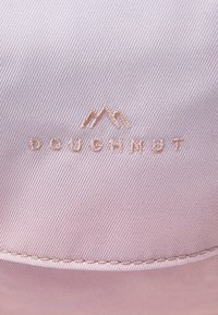 Jasnoróżowa tkanina z wypukłym, złotym haftowanym logo z górskimi akcentami oraz słowem "DOUGHNUT" w czystej, nowoczesnej czcionce.