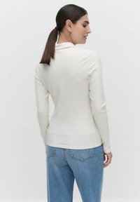 Pitkähihaista ribbikangasta oleva paita off-white väriin, jossa on hillitty kaula-aukko ja slim fit -malli, yhdistettynä korkeavyötäröisiin vaaleansinisiin farkkuihin.