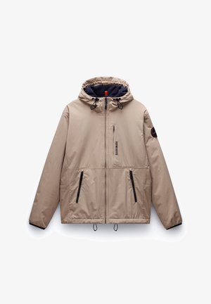 Beige kapjesjas met een gladde buitenkant, marineblauwe voering, zwarte accenten, twee voorste ritszakken en koordjes aan de onderkant en de capuchon.