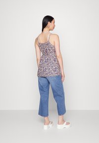 Camisola de alças com estampado floral e alças ajustáveis, vestida sobre jeans de denim azul largos, combinada com sapatos de plataforma brancos e grossos.