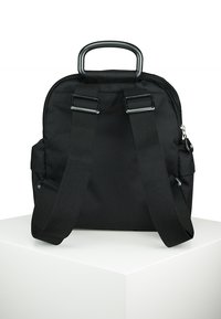 Zaino in tessuto nero con design arrotondato, manico superiore, spallacci regolabili e chiusura con zip. Presenta un materiale testurizzato e dettagli minimalisti.