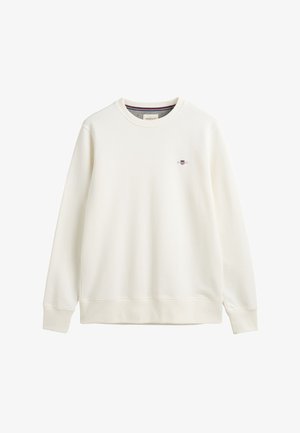 Krémová mikina vyrobená z mäkkého materiálu, s okrúhlym výstrihom a rebrovanými manžetami. Malé logo je umiestnené na ľavej strane hrudi.