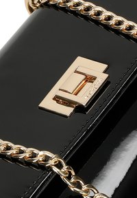Schwarze Lackleder-Handtasche mit einem goldenen Kettenriemen und einem rechteckigen metallenen Verschluss mit eingravierten Details. Glatte Textur, schlankes Design.