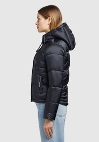 Giacca a puffo nera con cappuccio, con chiusura frontale con zip, tasche laterali e design trapuntato. Realizzata in un tessuto liscio e lucido.