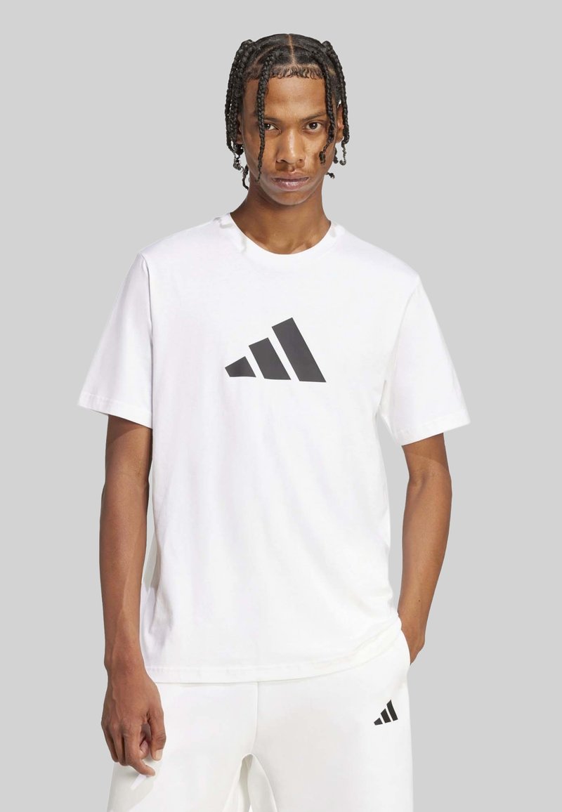 Camiseta blanca de manga corta con un gran logo negro de Adidas en el frente. Hecha de tela suave, con cuello redondo y un corte relajado.