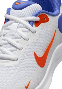 Sneakers Nike s převážně bílým síťovaným svrškem a modrými akcenty, doplněné jasně oranžovými „swish“ prvky. Šňůrky jsou bílé, textura je hladká.