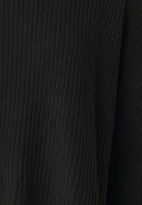 Pulover negru dintr-un tricot cu o textură cu nervuri, croială lejeră și decolteu larg. Țesătura pare moale și elastică.