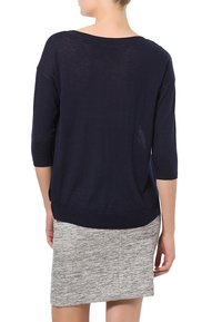 Marineblaues Strickpullover mit Dreiviertelärmeln, lockerer Passform und weitem Rundhalsausschnitt, kombiniert mit einem hellgrauen, strukturierten Bleistiftrock.