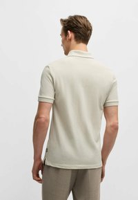 Polo shirt beige chiaro con maniche corte, texture morbida e colletto classico. Presenta uno spacco laterale in fondo e un branding discreto.