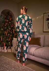 Zelený pyžamový set s vianočnými vzormi Santa Clausa. Obsahuje mikinu a nohavice s rebrovanými manžetami, vyrobené z mäkkej látky, vhodné na zimu.
