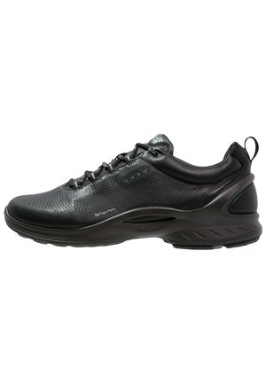 Scarpa sportiva nera con tomaia in pelle perforata, collo imbottito e suola testurizzata con punti di accento verdi e cuciture dettagliate.