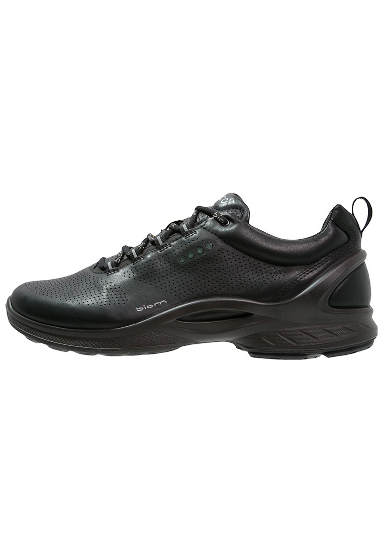 Scarpa sportiva nera con tomaia in pelle perforata, collo imbottito e suola testurizzata con punti di accento verdi e cuciture dettagliate.