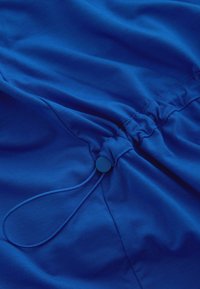 Material albastru cu un șnur strâns, prevăzut cu un toggle rotund. Textură netedă, cu o culoare uniformă și detalii de coasere minime.