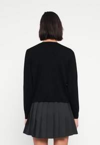 Μαύρο πλεκτό πουλόβερ με μακριά μανίκια, στρογγυλή λαιμόκοψη και άνετη γραμμή, συνδυασμένο με γκρι πλισέ φούστα.