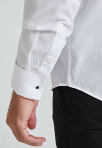 Poignet de chemise blanche avec un détail de bouton, featuring un bouton noir contrastant, texture lisse et design à manches longues.
