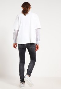 Bílý oversize tričko vrstvené přes pruhované dlouhý rukáv, spárované s úzkými černými džíny a bílými teniskami. Jednoduchý design, ležérní střih.