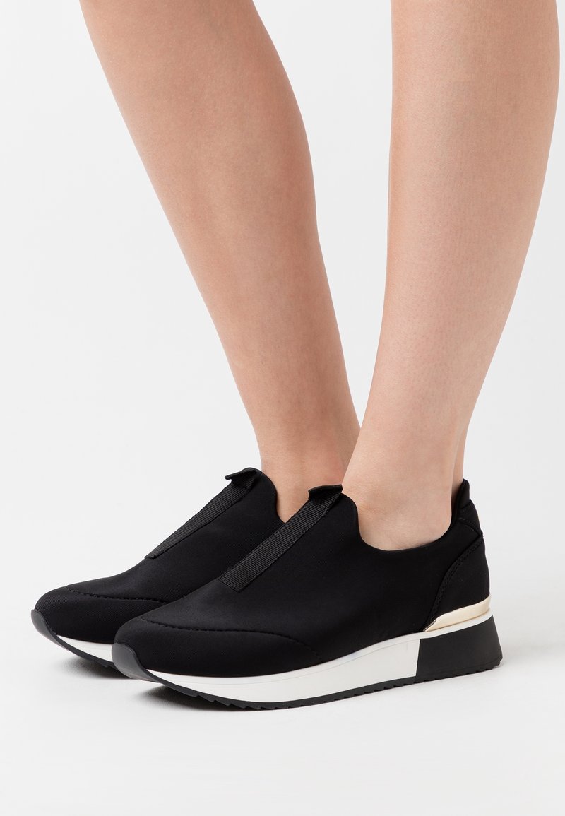 Svarta slip-on skor med en slät textilöverdel, rund tå och vit mellansula. Utrustad med texturerade sidodetaljer och elastiska remmar för bättre passform.