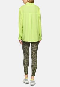 Fluorescent green, long-sleeve shirt paired with olive leopard-print leggings and grey sneakers, featuring zip accents at the ankle.