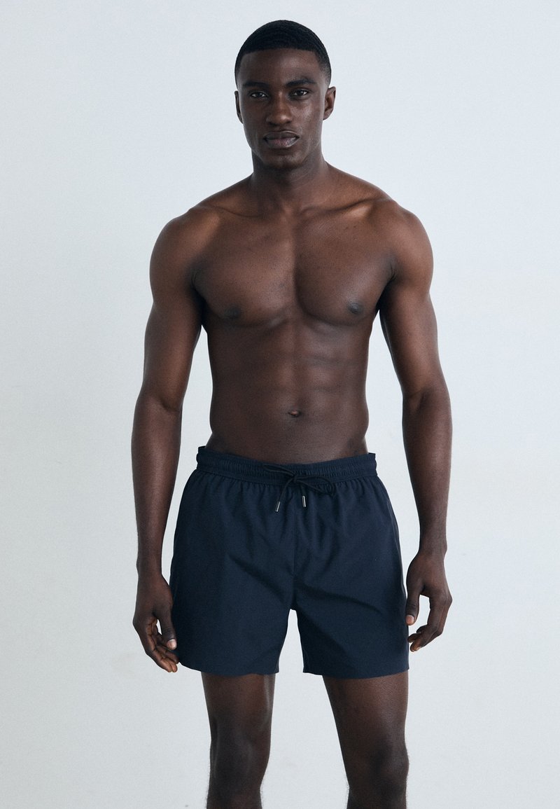 Schwarze Badehosen mit elastischem Bund und Kordelzugverschluss, aus leichtem Stoff gefertigt, zeichnen sich durch ein einfaches, klassisches Design aus.