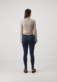 Suéter de punto colorido y cortado con un acabado texturizado y bordes con volantes, combinado con unos jeans ajustados de mezclilla oscura y sandalias de plataforma.
