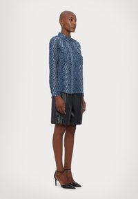 Blå slangeprintbluse med krave og lange ærmer, parret med sorte faux lædershorts og spidse sorte hæle.