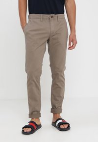 Jasnobrązowe chinosy o prostych nogawkach, z zapięciem na guzik i bocznymi kieszeniami. Noszone z czarno-białymi sandałami z kolorowymi akcentami.