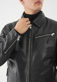 Černá kožená bunda s límcem, několika zipovými kapsami a hladkou texturou. Obsahuje stříbrné zipy a akcenty.