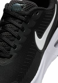 Scarpa da atletica nera con tomaia in mesh, sovrapposizioni sintetiche testurizzate, logo Nike bianco prominente e una suola intermedia bianca con accenti a motivo.