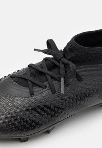 Schwarzer Fußballschuh mit strukturiertem Design, passgenauem, sockenähnlichem Sitz, flachen Schnürsenkeln und geformten Noppen an der Sohle für besseren Halt.