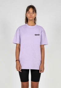 Lys lilla bomulds t-shirt med rund hals og korte ærmer, med sort tekst på venstre side. Sammen med sorte cykelshorts.