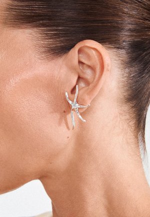 Close-up of a person's ear wearing a shiny silver starfish-shaped earring with five textured arms.