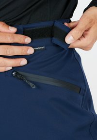 Mörkblå byxor med kardborreband och en ficka med dragkedja i svart. Slät textur och lättviktigt tyg.