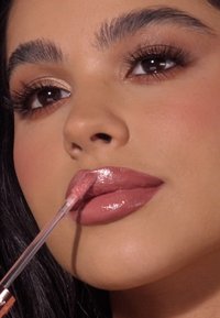 Lipgloss in een zachte roze tint, met een dikke en glanzende textuur, aangebracht met een doe-foot applicator; gladde lippen met gedefinieerde contouren.