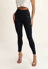 Leggings neri con una vita alta, realizzati in un tessuto liscio. Presentano un piccolo logo sulla coscia e un design aderente.